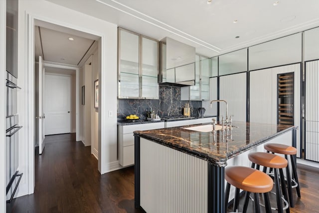 kitchen featuring sink, a kitchen island with sink, dark hardwood / wood-style floors, crown molding, and decorative backsplash