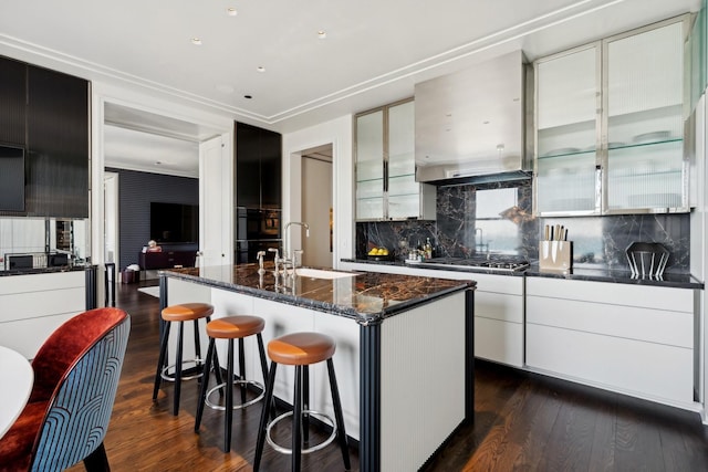 kitchen featuring sink, dark hardwood / wood-style flooring, stainless steel gas stovetop, decorative backsplash, and a center island with sink