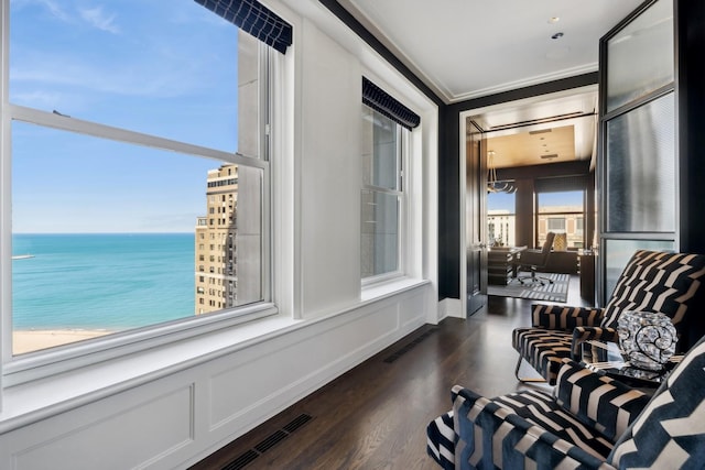 sitting room featuring crown molding, a water view, dark wood-type flooring, and a beach view