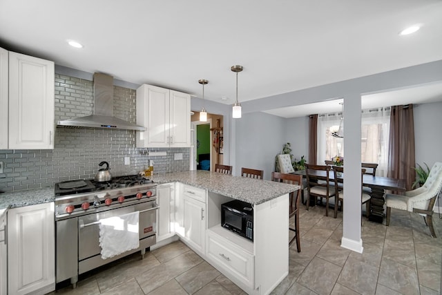 kitchen with kitchen peninsula, tasteful backsplash, wall chimney range hood, range with two ovens, and white cabinetry