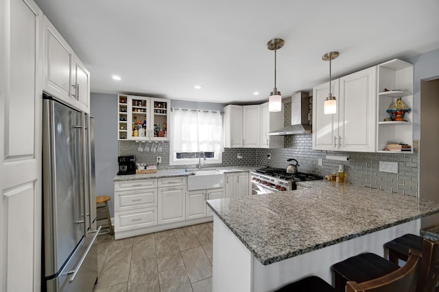 kitchen featuring stove, white cabinets, wall chimney range hood, high quality fridge, and kitchen peninsula