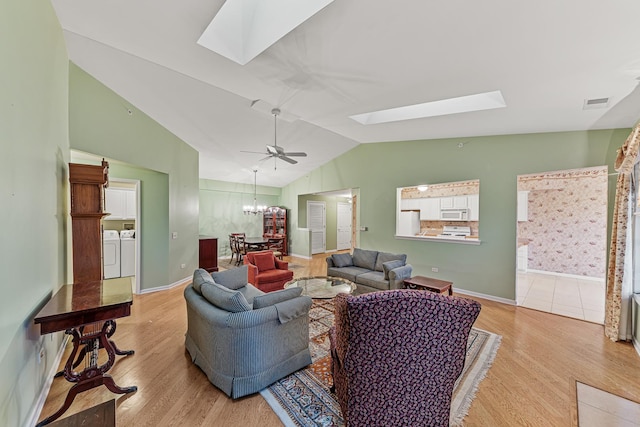 living room featuring lofted ceiling with skylight, light hardwood / wood-style flooring, washer and dryer, and ceiling fan with notable chandelier