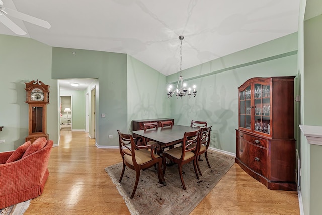 dining space with ceiling fan with notable chandelier, light hardwood / wood-style floors, and vaulted ceiling