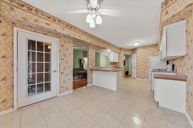 kitchen featuring white stove, white cabinets, ceiling fan, light tile patterned flooring, and kitchen peninsula