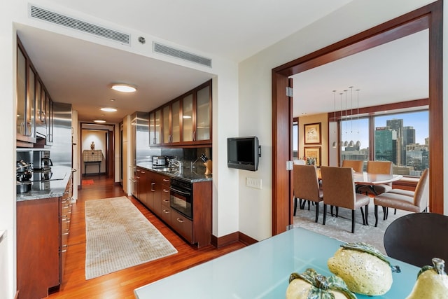 kitchen with black oven, hardwood / wood-style floors, dark stone counters, and sink