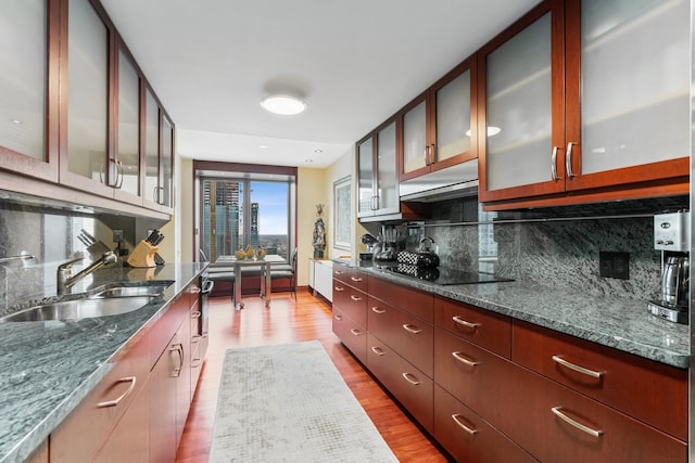 kitchen featuring decorative backsplash, black electric stovetop, light wood-type flooring, dark stone counters, and sink