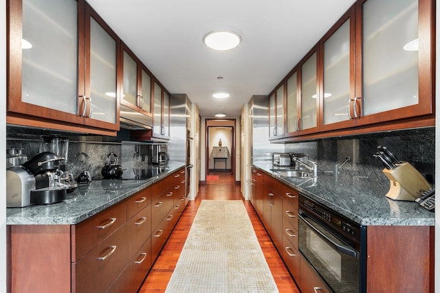 kitchen featuring dark stone countertops, black electric cooktop, sink, and tasteful backsplash