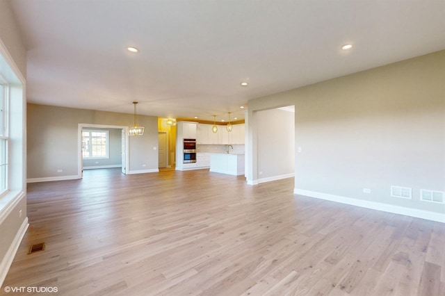 unfurnished living room with light hardwood / wood-style floors, an inviting chandelier, and sink