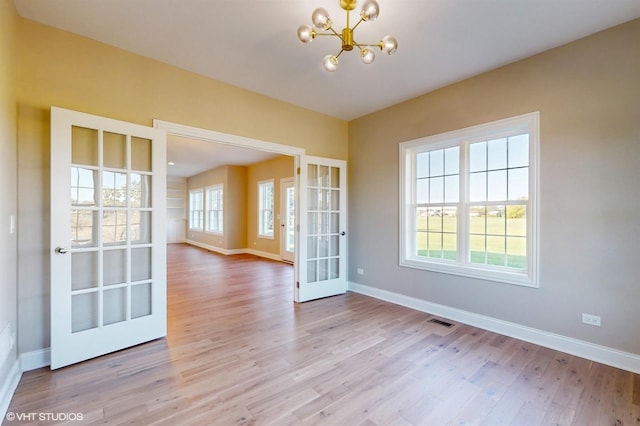 unfurnished dining area with french doors, light wood-type flooring, and a notable chandelier