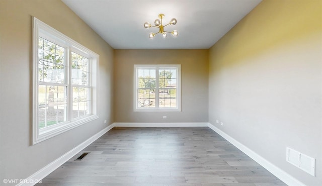 spare room with a healthy amount of sunlight, light hardwood / wood-style floors, and a chandelier