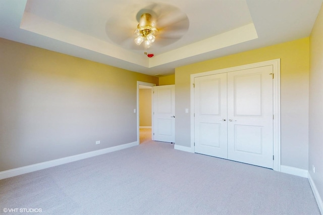 unfurnished bedroom featuring carpet, a closet, a raised ceiling, and ceiling fan