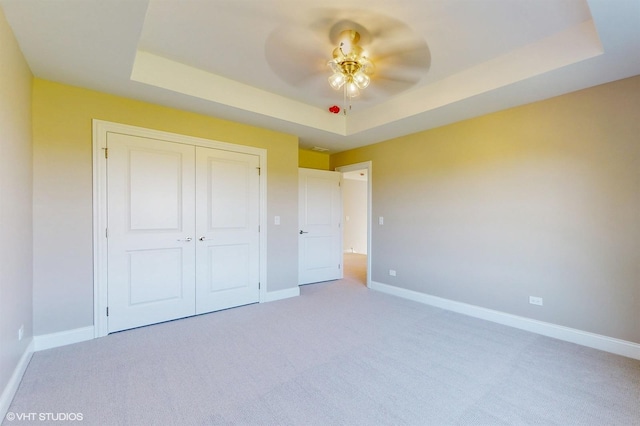 unfurnished bedroom with a tray ceiling, ceiling fan, a closet, and carpet flooring