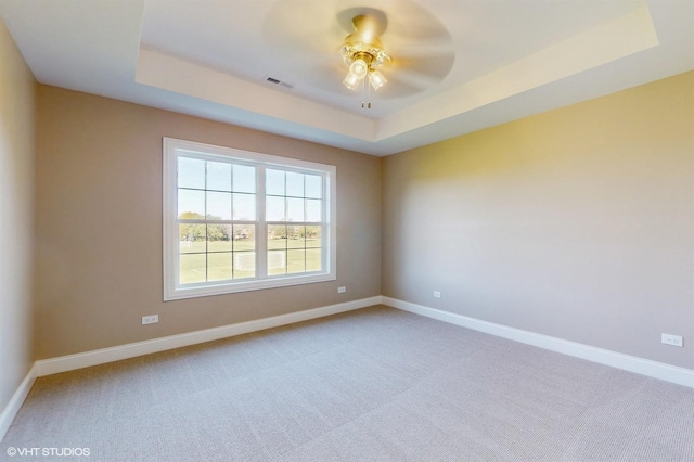 empty room with carpet flooring, ceiling fan, and a raised ceiling