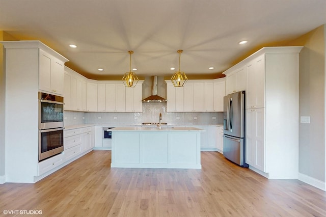 kitchen featuring white cabinets, wall chimney exhaust hood, stainless steel appliances, and decorative light fixtures