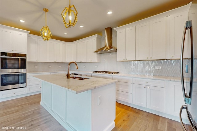 kitchen featuring white cabinetry, sink, hanging light fixtures, and wall chimney range hood