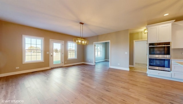 interior space featuring tasteful backsplash, double oven, decorative light fixtures, light hardwood / wood-style flooring, and white cabinetry