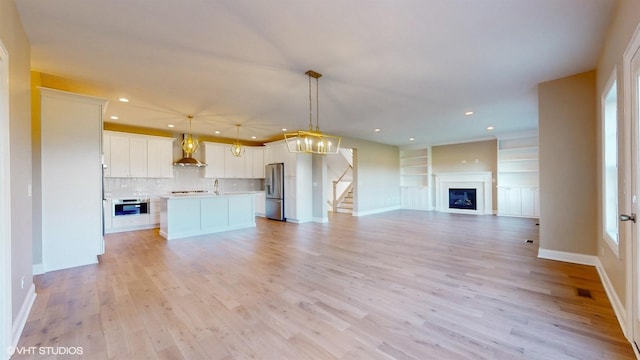 unfurnished living room featuring built in shelves, sink, and light wood-type flooring