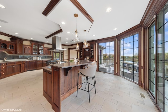 kitchen featuring crown molding, hanging light fixtures, a kitchen island, light stone countertops, and island range hood