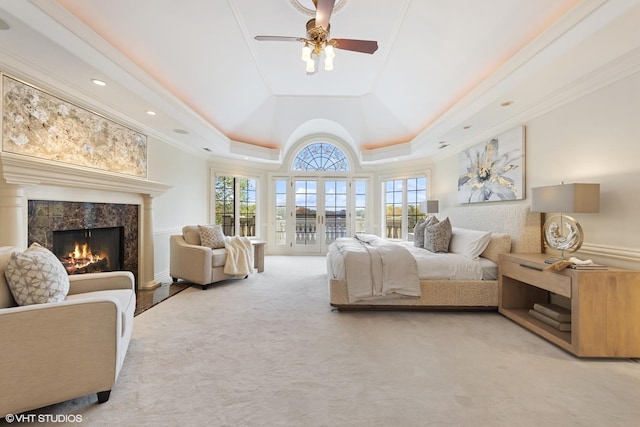 carpeted bedroom with a tray ceiling, a tile fireplace, ceiling fan, and crown molding