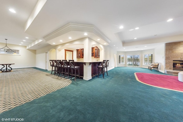 interior space featuring a tile fireplace, bar area, a tray ceiling, and dark carpet