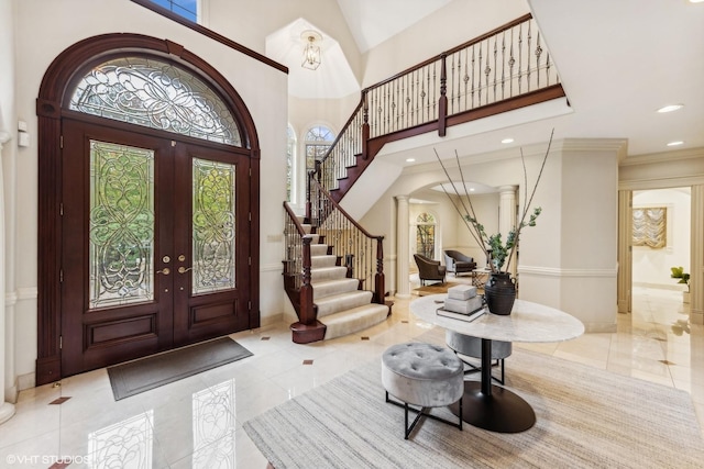 entrance foyer with ornate columns, crown molding, a high ceiling, and french doors