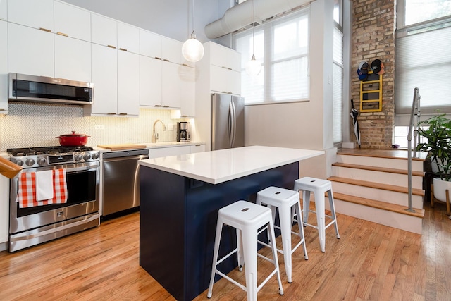 kitchen featuring hanging light fixtures, appliances with stainless steel finishes, a kitchen breakfast bar, a kitchen island, and light hardwood / wood-style floors