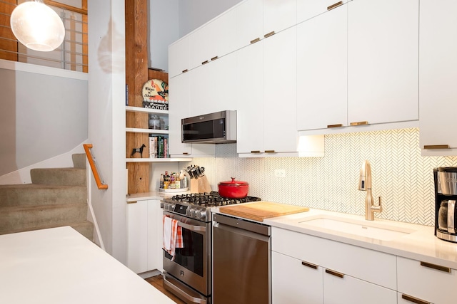 kitchen featuring appliances with stainless steel finishes, white cabinetry, sink, decorative backsplash, and hanging light fixtures