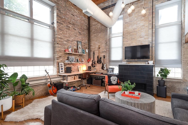 living room featuring a fireplace, a towering ceiling, wood-type flooring, and brick wall