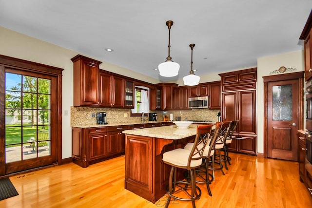 kitchen with light stone countertops, light wood-type flooring, paneled fridge, a center island, and hanging light fixtures