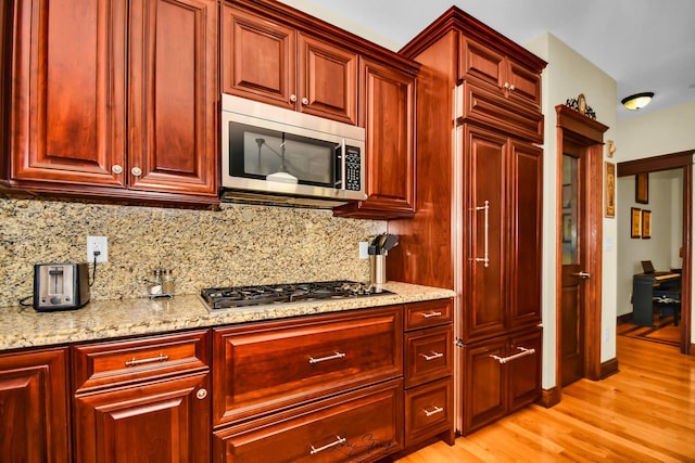 kitchen featuring decorative backsplash, light wood-type flooring, stainless steel appliances, and light stone counters