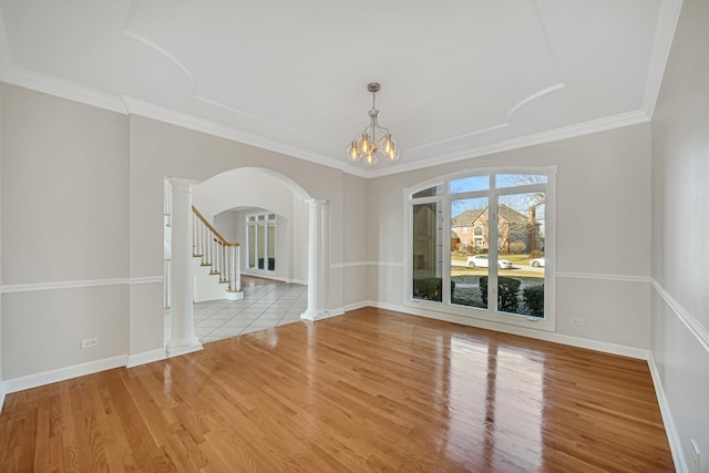 unfurnished room featuring a notable chandelier, light hardwood / wood-style floors, ornamental molding, and decorative columns