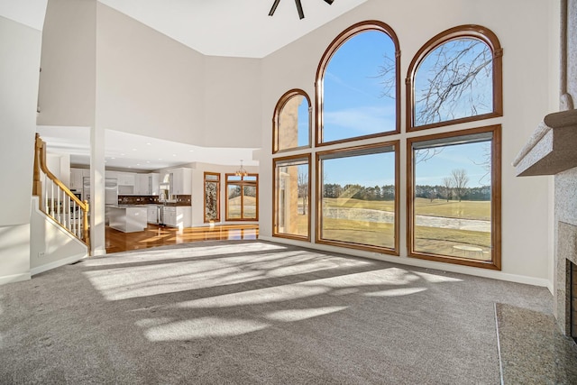 unfurnished living room featuring ceiling fan with notable chandelier, a fireplace, carpet floors, and a high ceiling