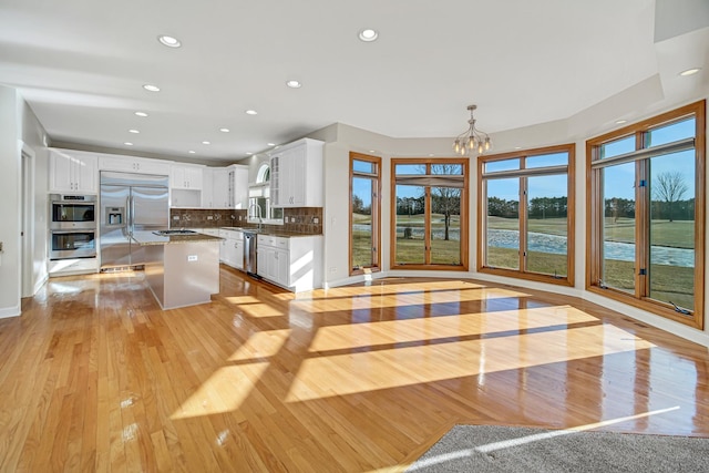 kitchen with stainless steel appliances, white cabinets, backsplash, decorative light fixtures, and a water view