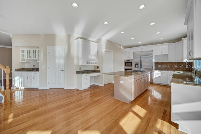 kitchen with white cabinetry, a center island, stainless steel appliances, dark stone counters, and light hardwood / wood-style floors