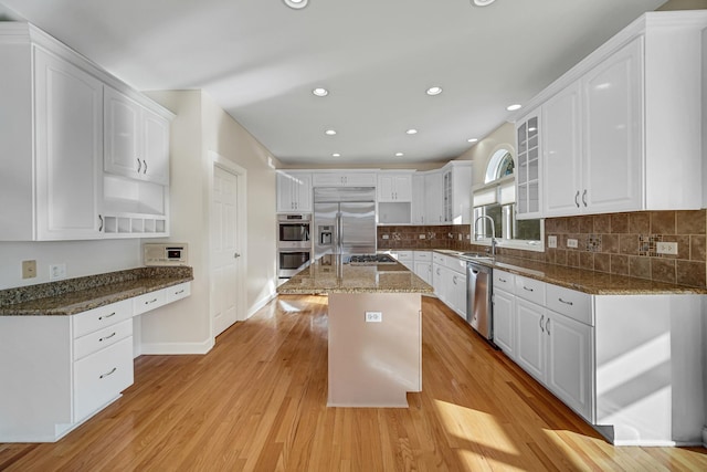 kitchen with a center island, white cabinets, dark stone countertops, appliances with stainless steel finishes, and light hardwood / wood-style floors