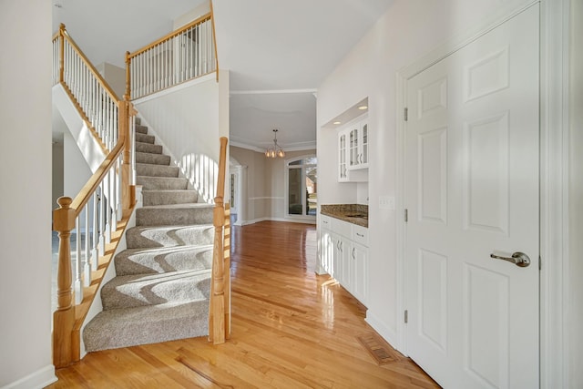 stairway featuring wood-type flooring, ornamental molding, and an inviting chandelier