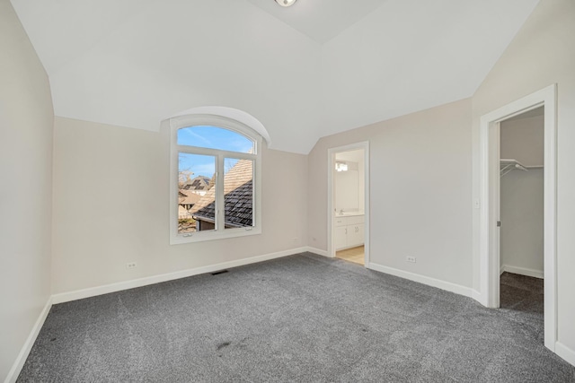 unfurnished bedroom with a walk in closet, a closet, ensuite bath, and vaulted ceiling