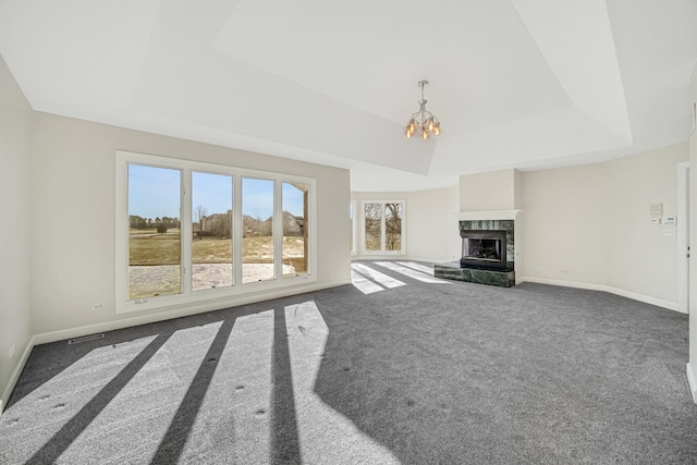 unfurnished living room with a raised ceiling, a premium fireplace, dark carpet, and an inviting chandelier