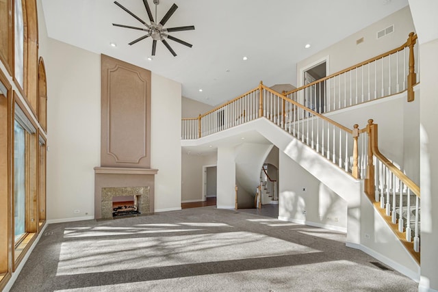 unfurnished living room featuring carpet flooring, ceiling fan, a large fireplace, and a high ceiling