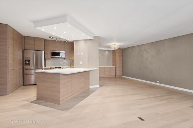 kitchen with a notable chandelier, appliances with stainless steel finishes, light hardwood / wood-style floors, and backsplash