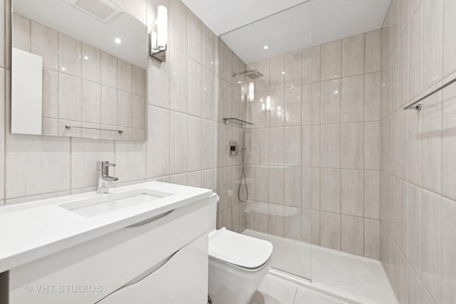 bathroom featuring vanity, toilet, tile walls, and a tile shower