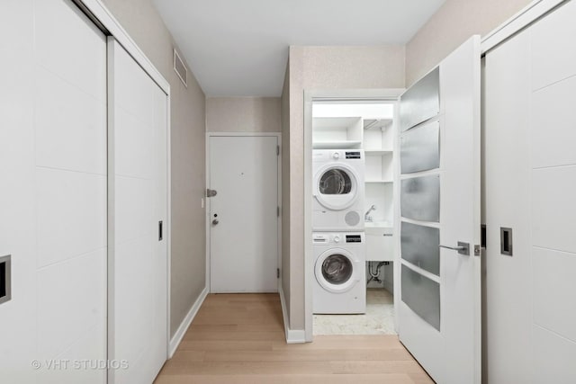 washroom with stacked washer and dryer and light hardwood / wood-style flooring