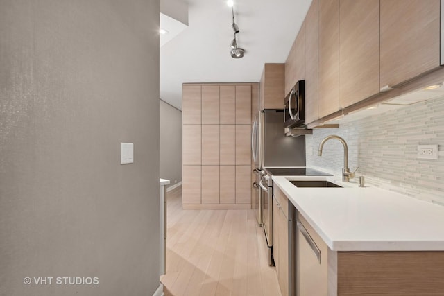 kitchen with sink, light hardwood / wood-style flooring, rail lighting, appliances with stainless steel finishes, and decorative backsplash