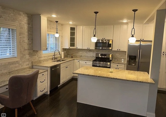 kitchen with appliances with stainless steel finishes, light stone counters, sink, decorative light fixtures, and white cabinets