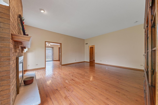 unfurnished living room featuring ceiling fan, light wood-type flooring, and a brick fireplace