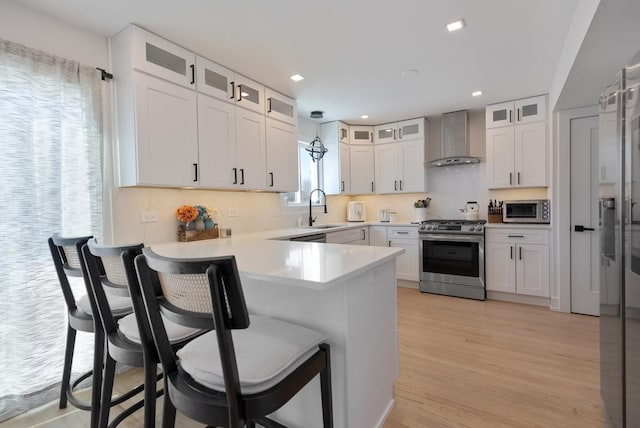 kitchen featuring a kitchen breakfast bar, white cabinetry, stainless steel appliances, wall chimney exhaust hood, and light hardwood / wood-style flooring