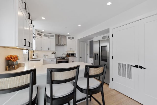 kitchen with a barn door, appliances with stainless steel finishes, light wood-type flooring, wall chimney exhaust hood, and white cabinetry