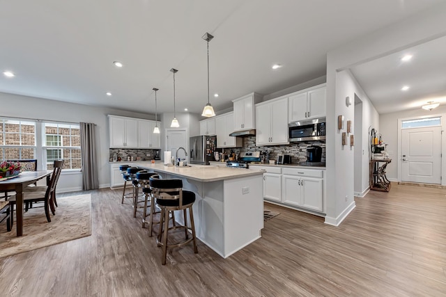 kitchen with white cabinets, hanging light fixtures, stainless steel appliances, and a kitchen island with sink