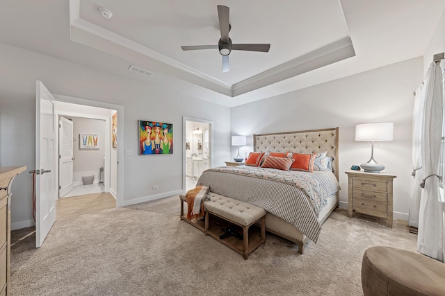 bedroom with light carpet, a tray ceiling, ensuite bath, and ceiling fan