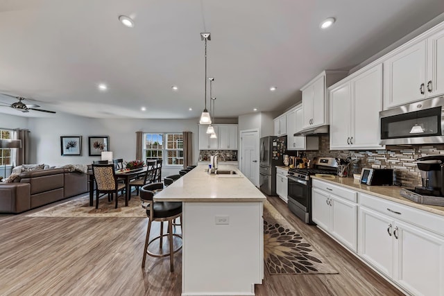 kitchen with a kitchen island with sink, hanging light fixtures, decorative backsplash, white cabinets, and appliances with stainless steel finishes